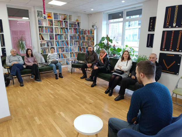 Eine Gruppe von Menschen, die um einen Tisch in einem Raum mit Bücherregalen, Pflanzen und einem Fenster sitzen und während eines Workshops über die Zukunft von Gesundheit und Wohlbefinden in Berlin, Deutschland, diskutieren.