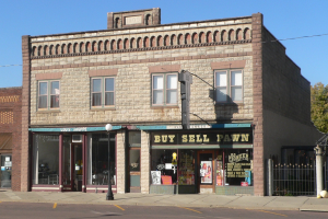 Ein Gebäude mit einem "Kaufen Verkaufen Pfandleihe"-Schild an einer Straßenecke, umgeben von Straßeninfrastruktur und Grün unter einem klaren Himmel.