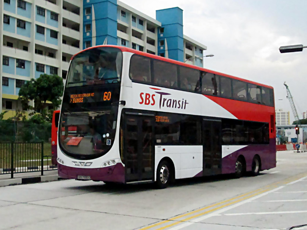 Ein elektrischer Bus steht im Mittelpunkt der Szene mit einem Gebäude im Hintergrund, Bäumen vor dem Gebäude und einem Zaun auf der rechten Seite des Fußwegs, unter einem Himmel.
