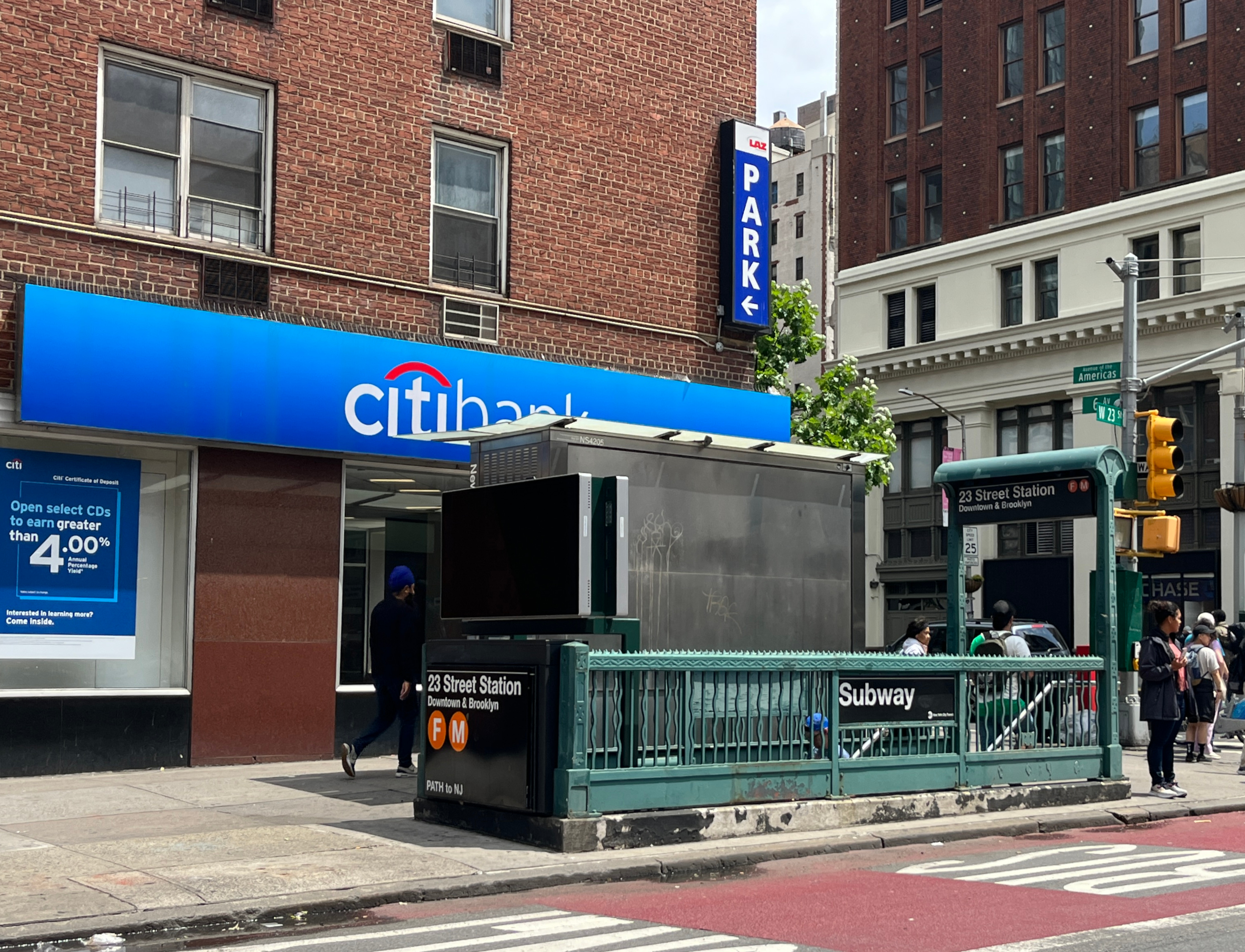 Eine belebte Stadtstraße mit Fußgängern, Gebäuden, einem Citibank-Bushaltestellen-Schild im Vordergrund und einem bewölkten Himmel.