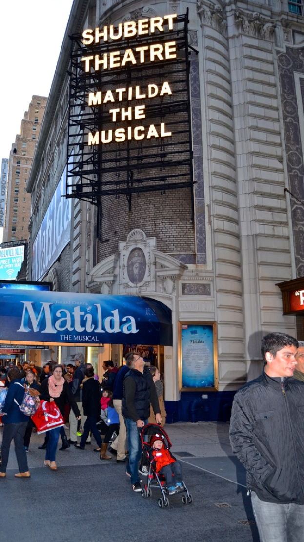 Eine Gruppe von Menschen in der Nähe von Gebäuden und Werbetafeln mit einem Baby im Kinderwagen.