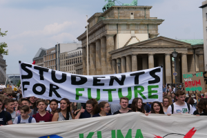 Eine Gruppe von Schülern marschiert in Berlin mit einem bunt bemalten Banner, auf dem "Schüler für die Zukunft" steht, vor dem Hintergrund von Gebäuden, Bäumen und Himmel.