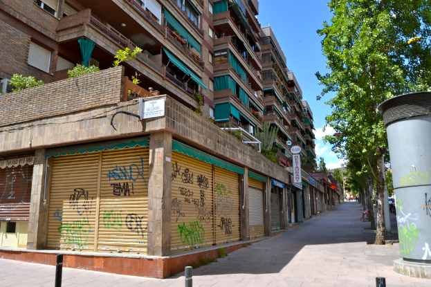 Eine Szene mit mehreren Gebäuden mit Fenstern, grünen Kleidungsstücken, Geschäften, Schildern und umliegenden Bäumen und Pflanzen.