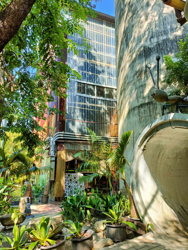 Ein Innenhof mit Topfpflanzen und Bäumen vor einem modernen, umweltfreundlichen Hotel, umgeben von Grün unter einem klaren blauen Himmel.