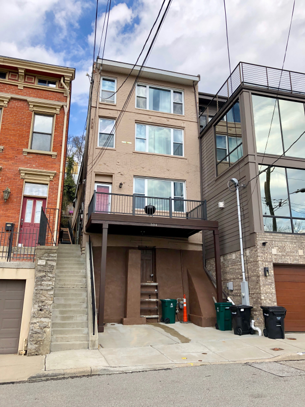 Eine Reihe von Stadthäusern an der 541 W 5th St, Chicago, mit Fenstern, Türen, Geländern, Treppen, Mülltonnen, einem Lichtmast, Drähten, Bäumen und einem bewölktem Himmel, die an der Ecke einer Straße mit einer Straße am unteren Ende des Bildes liegen.