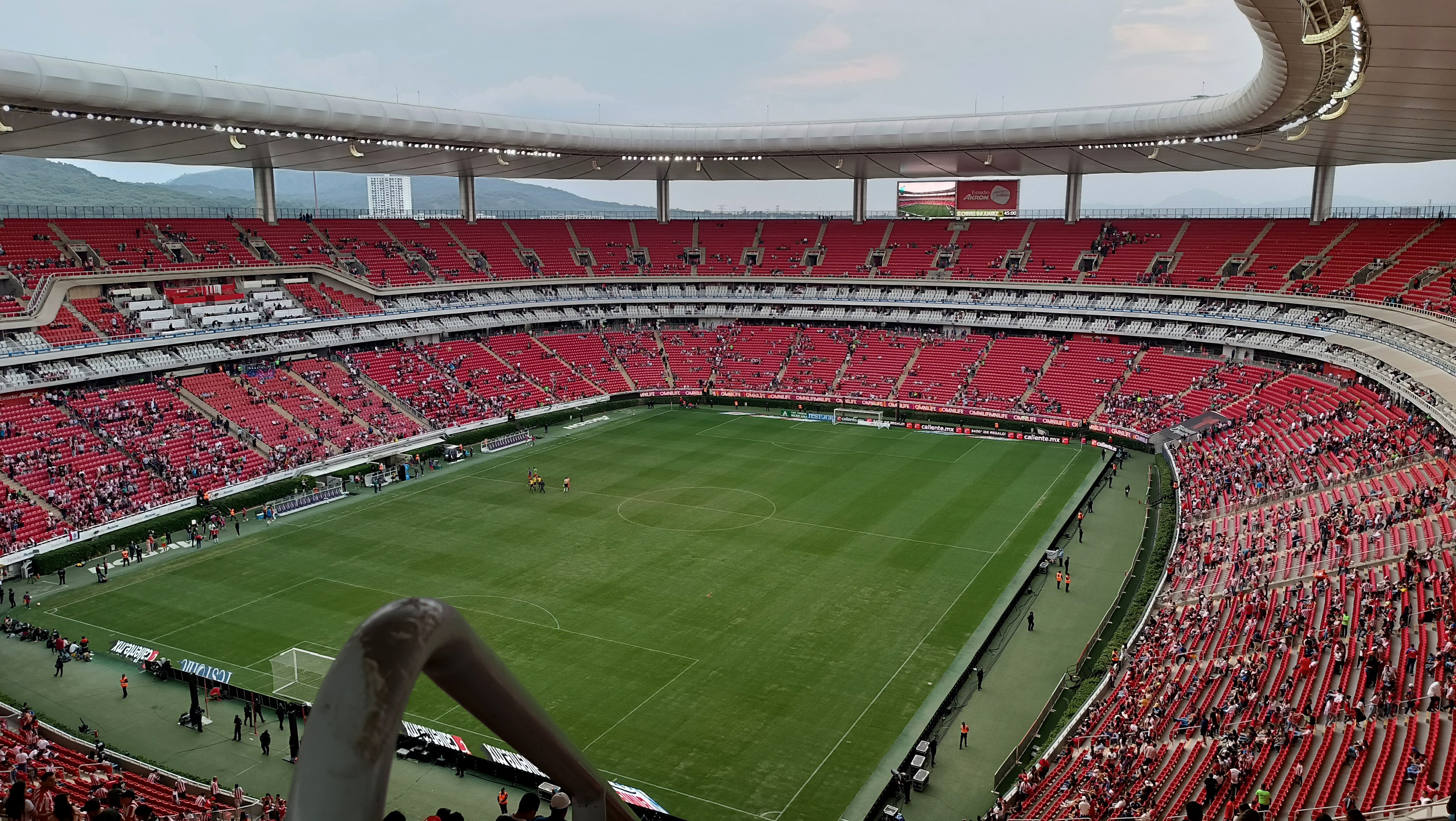 Großes Stadion voller Zuschauer bei einem Fußballspiel, mit Hügeln und einem klaren blauen Himmel im Hintergrund.