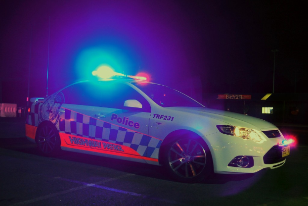 Ein weißer Polizeiwagen mit Leuchten und Aufklebern auf einem schwarzen Hintergrund.