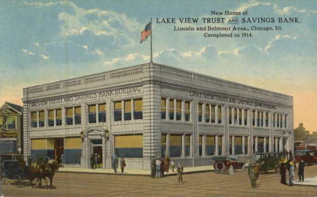 Schwarz-Weiß-Postkarte der Lake View Trust and Savings Bank an der Kreuzung Lincoln und Belmont Avenue in Chicago, Illinois, mit einer Gruppe von Menschen, einem Pferdewagen, frühen Automobilen, Bäumen und einer Fahne an einem bewölkten Tag.