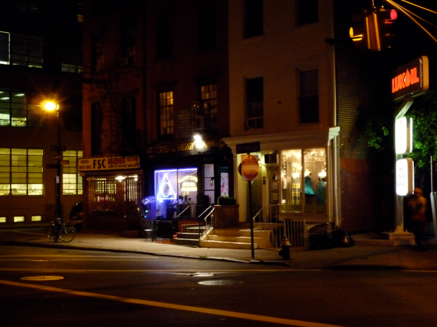 Eine Stadtstraßenszene mit Gebäuden, Geschäften, Bäumen, einer Straße, einem Fahrrad, Treppen und einer Ampel, alles beleuchtet von Lichtern.