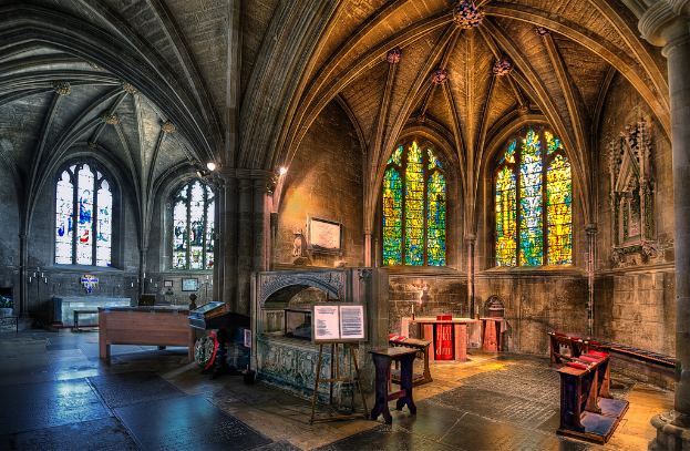 Ein Raum mit Bänken, Tischen, einer Tafel, Fenstern, einer Wand, Kerzen und einem Kamin in der Mitte, bearbeitet.