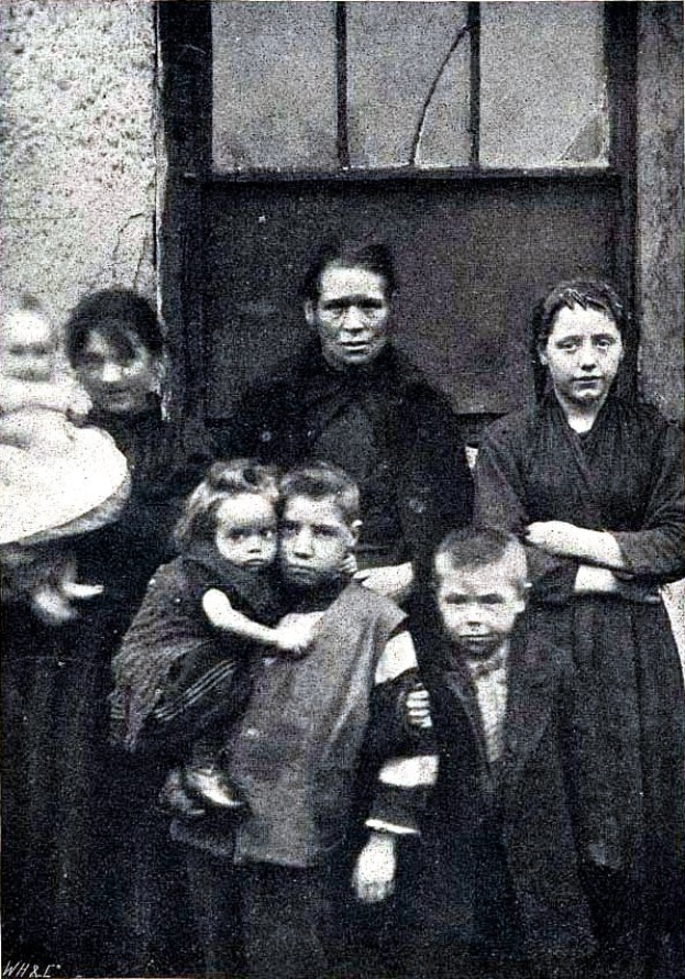 Schwarzes und weißes Foto einer Familie, die vor einer Wand mit einem Fenster posiert, mit Text unten, der 'Mother Teresa mit ihren Kindern' lautet.