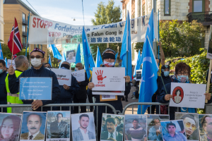 Eine Gruppe von Menschen mit Masken und Schildern und Plakaten steht vor einem Zaun mit Fotos und Text, protestiert in Istanbul, Türkei, mit Gebäuden, Bäumen und einem Laternenpfahl im Hintergrund.