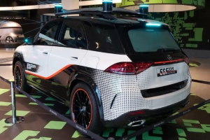 Mercedes-Benz E-Klasse Electric SUV auf der IAA in Frankfurt umgeben von Absperrpollern mit Seilen und Lichtern, mit einem weiteren Fahrzeug und einer textbedruckten Wand im Hintergrund.