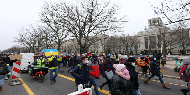 Eine große Gruppe von Menschen marschiert auf der Straße in Washington, D.C. am 21. Januar 2020 mit Schildern und Transparenten, während einige Fahrräder fahren, Schilder mit Stangen, Bäume und ein klarer blauer Himmel im Hintergrund.