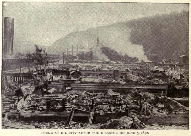 Schwarzes und weißes Foto einer Stadt nach der Katastrophe am 5. Juni 1892, das beschädigte Gebäude, Strommasten, Rauch und einen Hügel im Hintergrund zeigt.