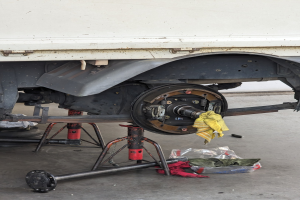 Ein gelber tuchbedeckter Lkw in einer Garage mit verstreuten Werkzeugen und Gegenständen auf dem Boden, was auf Wartungsarbeiten hindeutet.