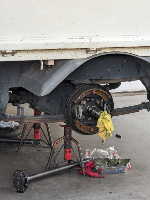 Ein gelber tuchbedeckter Lkw in einer Garage mit verstreuten Werkzeugen und Gegenständen auf dem Boden, was auf Wartungsarbeiten hindeutet.