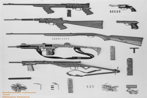 Schwarz-weiß-Foto von verschiedenen Waffen, Munition und verstreuten Gegenständen mit Text unten.