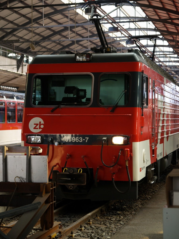 Ein Zug auf einem Bahngleis mit Steinen und Stangen in der Nähe und Text auf dem Zug.