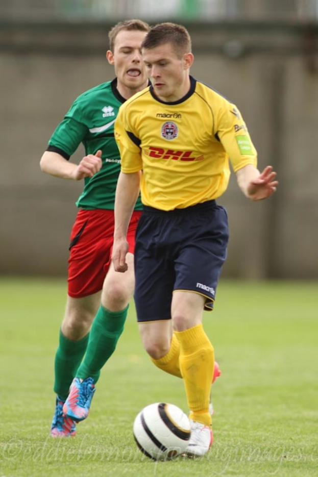Zwei Männer bei einem Fußballspiel auf einem grünen Feld mit einem Ball, mit unscharfem Hintergrund und Text unten.
