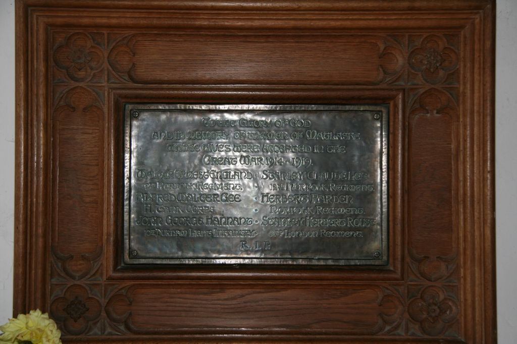 Eine Gedenktafel mit Text ist an einer braunen Wand oder einer Holztür angebracht, mit einem gelben Objekt, das einer Vase ähnelt, in der linken unteren Ecke.