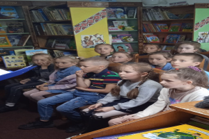 Eine Gruppe von Kindern sitzt in einer Bibliothek umgeben von Bücherregalen, mit einigen, die Bücher an Tischen auf beiden Seiten lesen.