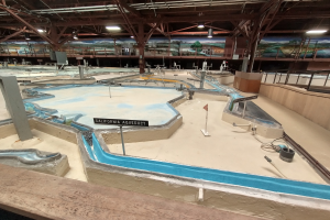 Großes Indoor-Wasserpark mit mehreren Wasserrutschen, Deckenbeleuchtung, Wandgemälden und einem Minigolf-Platz.