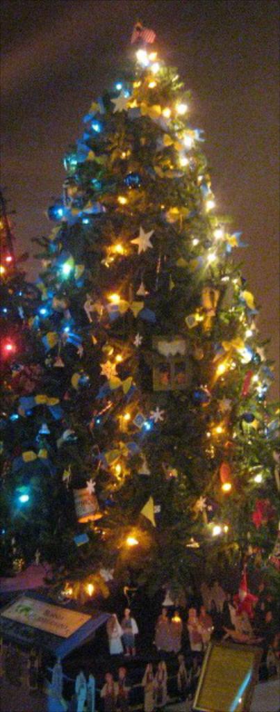 Ein geschmückter Weihnachtsbaum mit darunter auf einem Tisch platzierten Menschenfiguren.