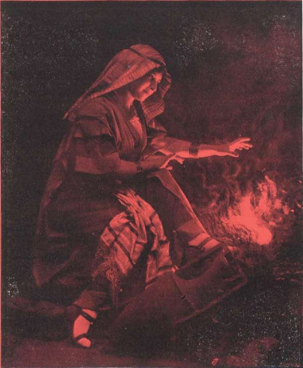 Ein altes Foto einer Frau, die vor einem Feuer sitzt und Schuhe trägt, mit einem dunklen Hintergrund.