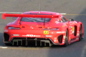 Ein leuchtend roter Porsche 911 GTS Rennauto mit schlankem, aerodynamischem Design, niedrigem Profil, breiter Basis, großem Spoiler, großem Heckflügel und großen schwarzen Rädern, das auf einer Rennstrecke fährt.