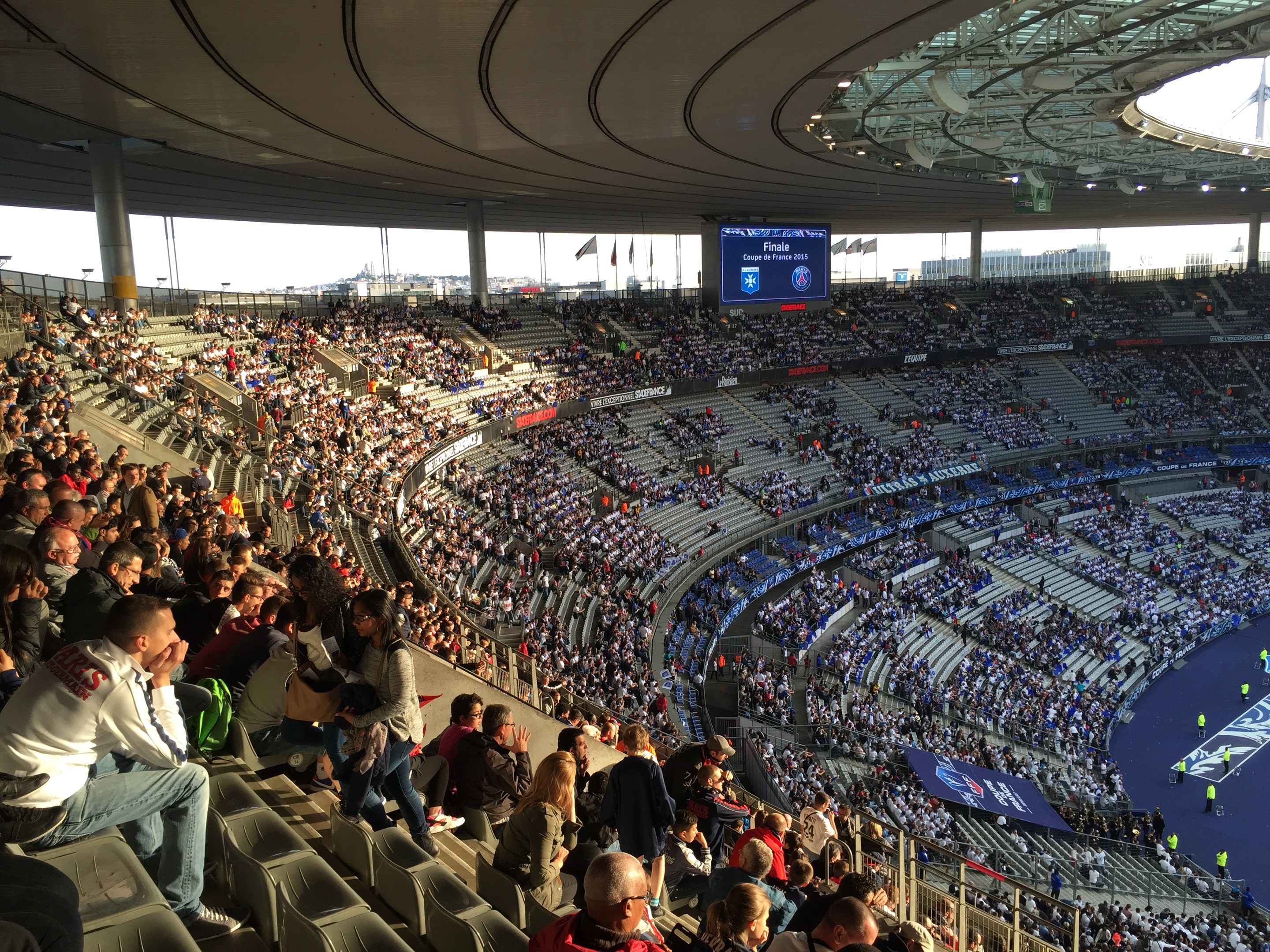 Große Zuschauermenge in einem Stadion bei einem Fußballspiel mit einer Bühne, Fahnen, Stangen und einem Bildschirm im Hintergrund