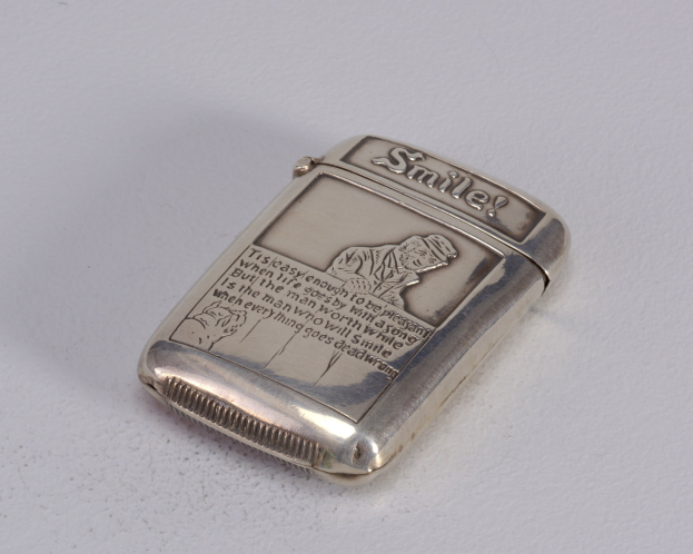 Silbernes Zigarettenetui mit einem Männerporträt darauf, auf einer weißen Oberfläche platziert, mit der Aufschrift "Feuerzeug".