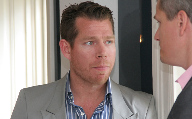 Zwei Männer in Blazern stehen vor einem Fenster mit einem Vorhang.