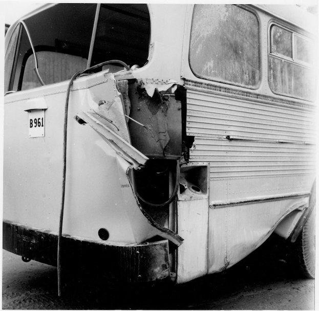 Schwarz-weiß-Foto eines Busses mit schwerer Frontschaden nach einem Autounfall auf der Straße.