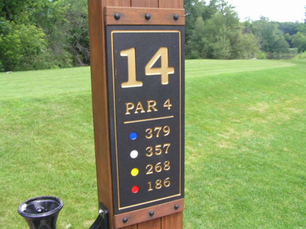 Ein hölzerner Pfahl mit Zahlen darauf steht vor einem grasbewachsenen Gebiet mit Bäumen.