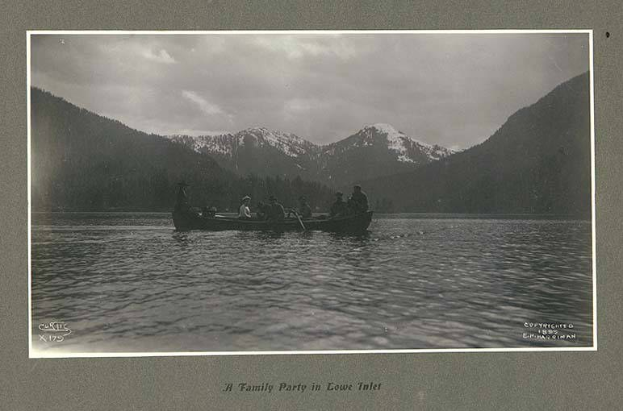 Schwarzes und weißes Foto einer Familie in einem Kanu auf einem See mit Bergen, Bäumen und Himmel im Hintergrund und Text unten.