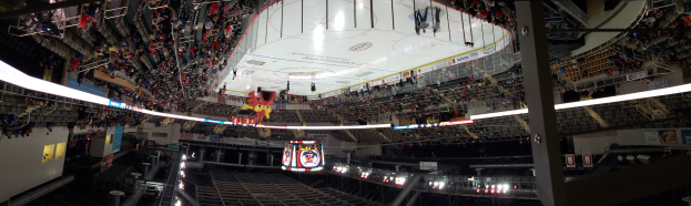 Eine große Arena voller Zuschauer bei einem Eishockeyspiel mit Stühlen, Geländern, Texttafeln, Lampen, Pfosten und einer Treppe, die zu den Sitzplätzen führt.