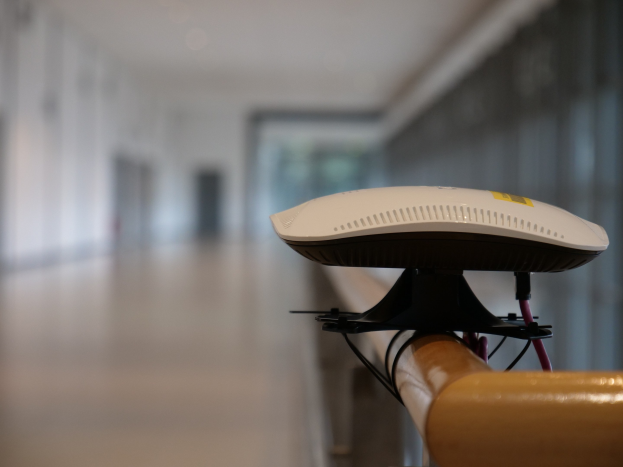 Weißer Router auf einem Holzgeländer in einem Flur mit unscharfem Hintergrund.