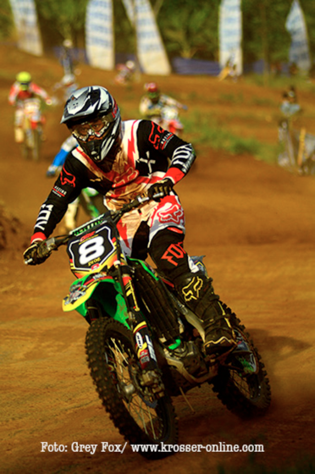 Mehrere Motorradfahrer mit Helm rasen, mit Text am unteren Bildrand.