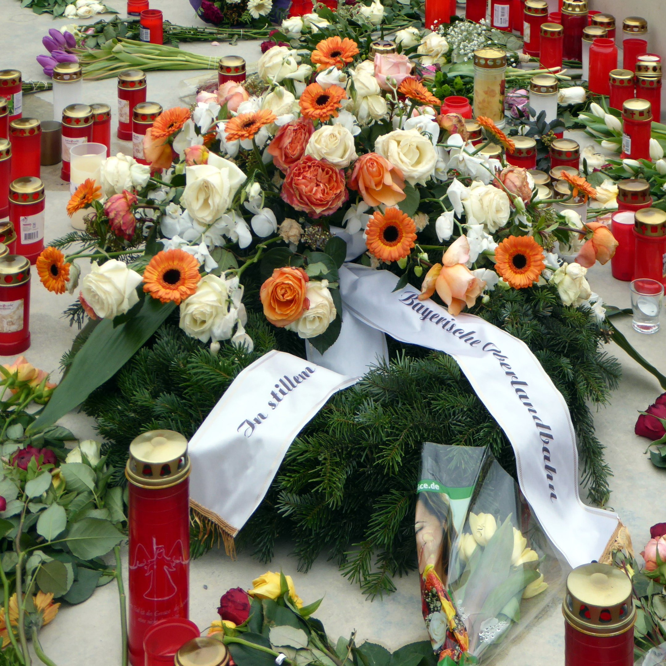 Ein Mahnmal in Berlin, Deutschland, mit Blumen und Kerzen, die vor einer Wand auf dem Boden plaziert sind.