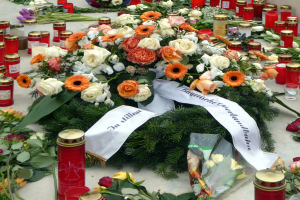 Ein Mahnmal in Berlin, Deutschland, mit Blumen und Kerzen, die vor einer Wand auf dem Boden plaziert sind.