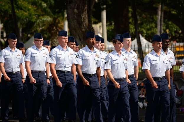 Männer in Uniform auf einer Straße mit einem Eisengeländer im Hintergrund.
