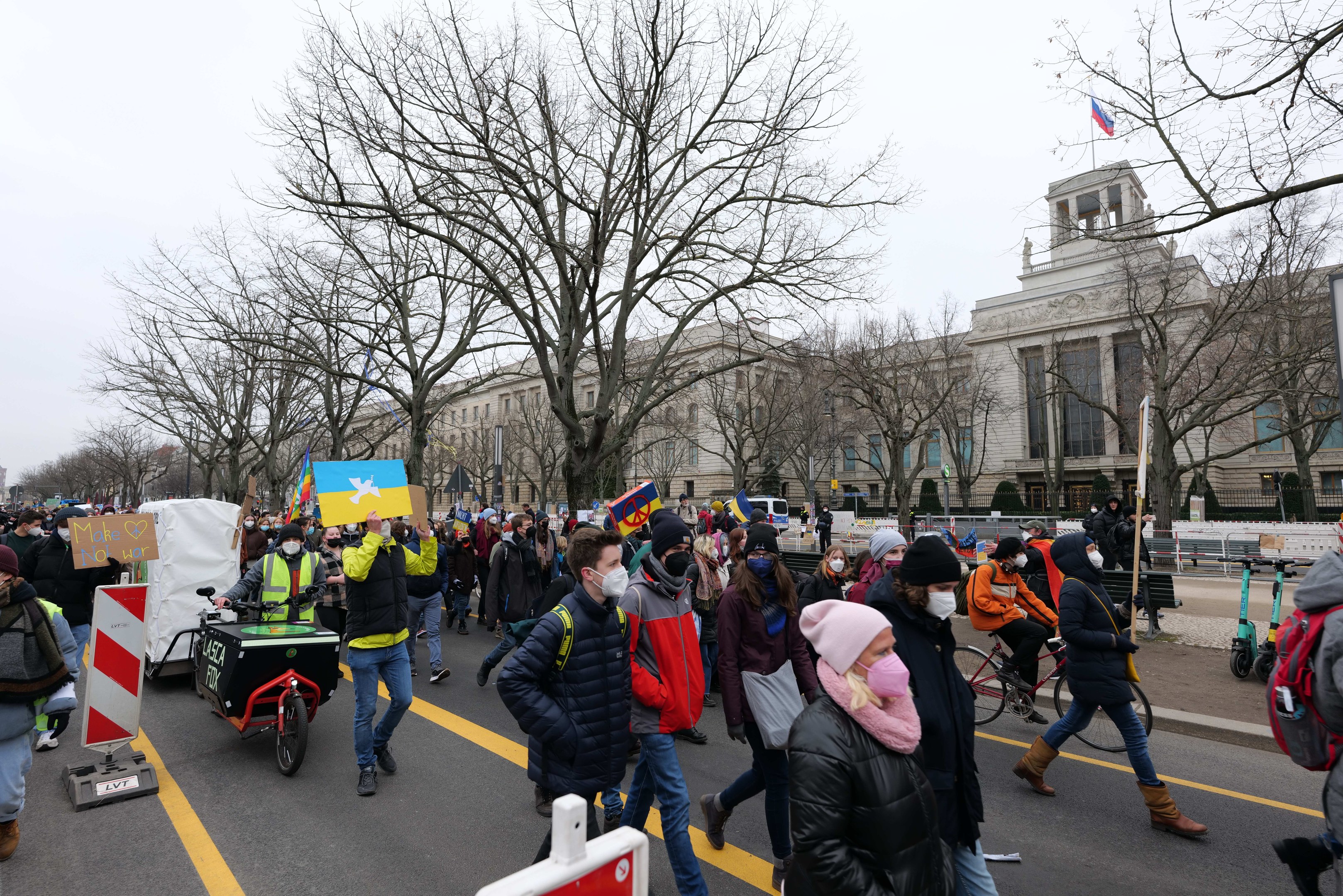 Eine große Gruppe von Menschen nimmt an einer Protestdemo in Washington, D.C. am 21. Januar 2020 teil und marschiert eine Straße entlang mit Schildern, Bannern und Fahrrädern vor einem Gebäude mit Schildern, Bäumen und einem klaren blauen Himmel.