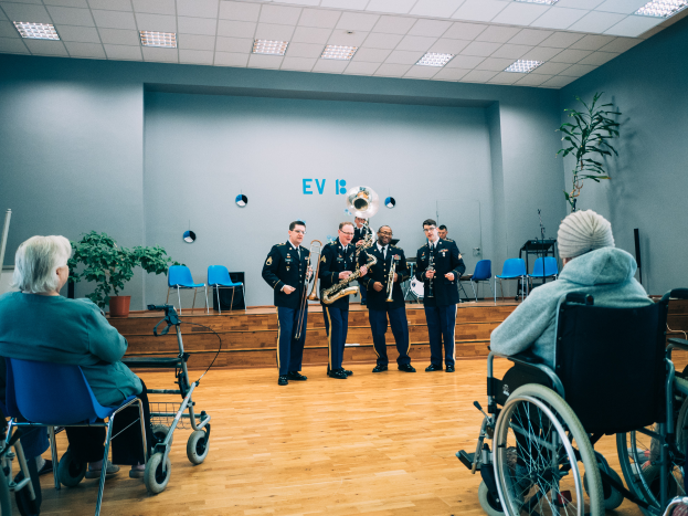 Eine Gruppe von Menschen in Rollstühlen, die in einem Raum mit Stühlen, Pflanzen und Deckenleuchten Musikinstrumente spielen, mit einigen Personen, die auf Stühlen sitzen, was auf ein Rollstuhlband-Event hindeutet.