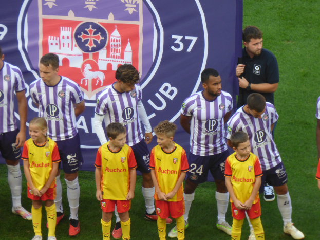 Eine Gruppe junger Jungs in Chivas de Guadalajara-Trikots, die zusammen auf einem Fußballfeld stehen, mit einem Banner im Hintergrund.
