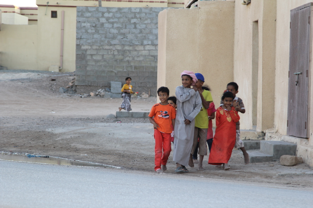 Eine Gruppe strahlender Kinder vor Gebäuden, Wasser, Felsen und einer Straße stehend.