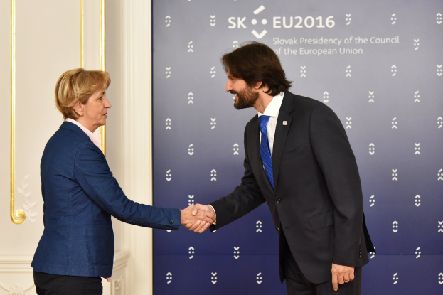 Bundeskanzlerin Angela Merkel und Bundespräsident Joachim Gauck schütteln sich vor einer Wand mit einem Banner 'EU-Gipfel' und einer Tür im Hintergrund die Hände, beide lächeln.