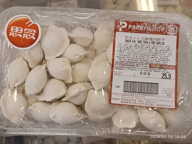 Ein Plastikbehälter mit einem Etikett, auf dem 'Park Shop' steht, enthält drei frische Schweineklöße, die mit einem Plastikdeckel abgedeckt sind und auf einem Tisch stehen.