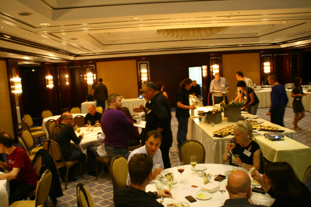 Ein Restaurantinnenraum mit Tischen und Stühlen, an denen Gruppen von Menschen sitzen und essen, und einige stehen um einen zentralen Tisch mit verschiedenen Speisen.