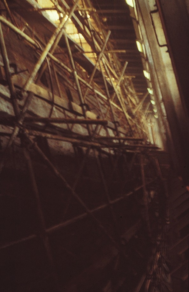 Ein Gebäude in Bau mit ausgedehntem Gerüst an der Seite, beleuchtet von Lichtern oben.